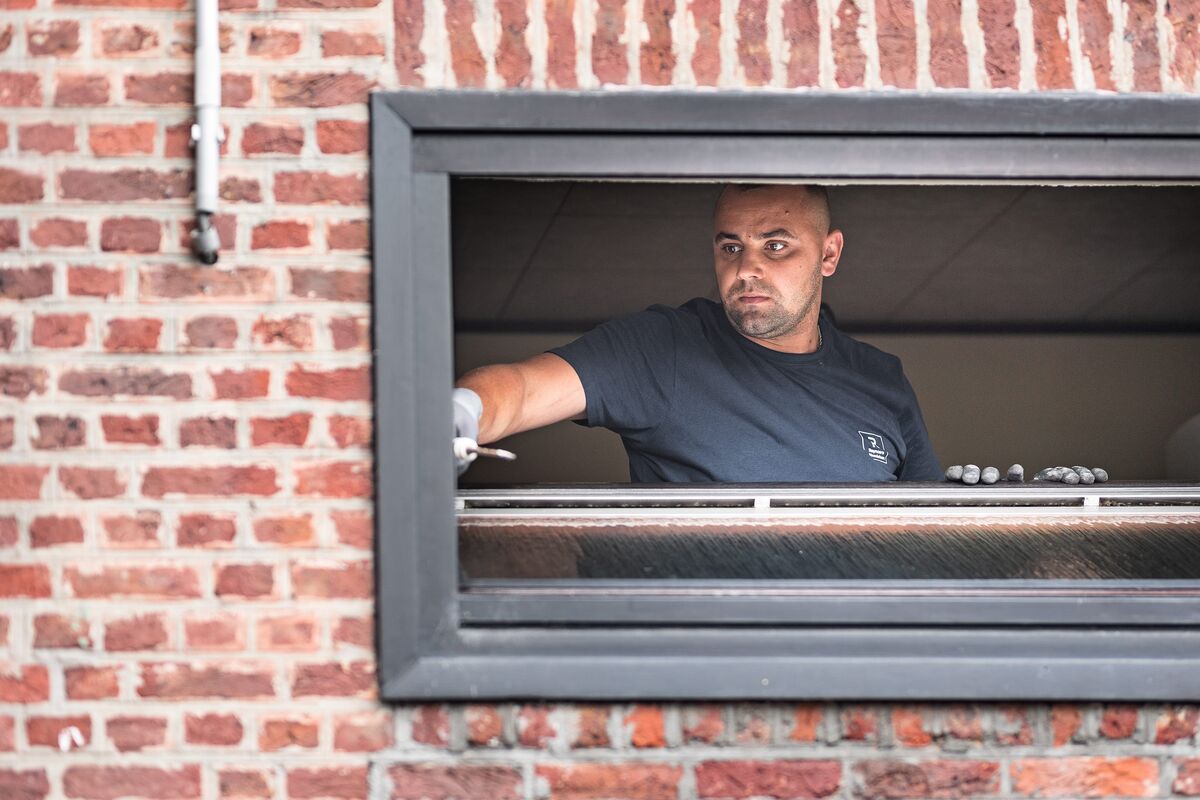 man installing window frame in brick wall