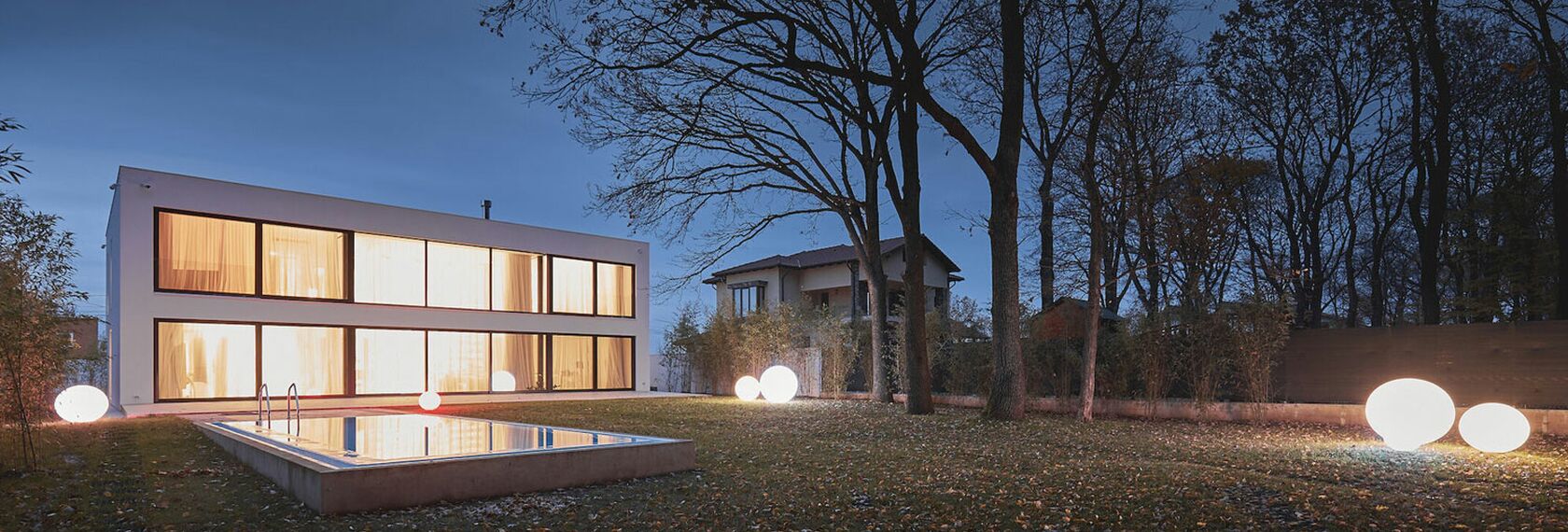 Outside view of white Romanian private home with bright lights shining through the windows.