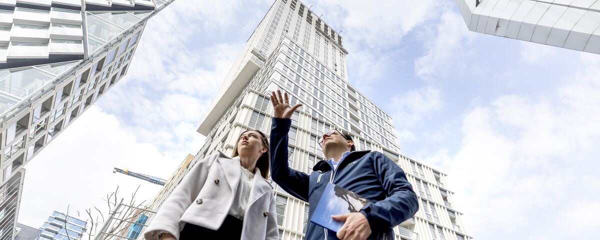 man and woman in front of skyscraper pointing at the sky