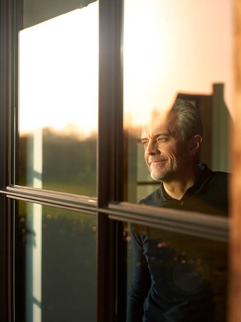 Middle-aged man looking out of window with warm sunlight.
