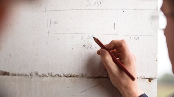 Man writing with pencil on concrete wall of construction site.